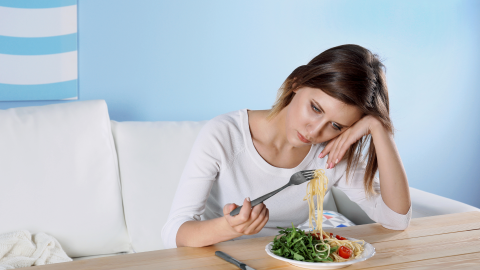 A sad woman stares at a plate of food. 